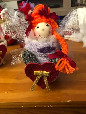 Muñeca de trenzas naranjas sentada sobre un corazón